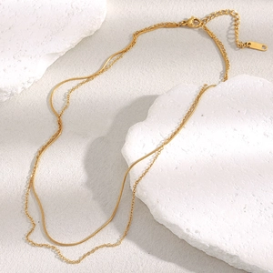 Detail of layered 18K gold-plated stainless steel snake and link chains on white stone