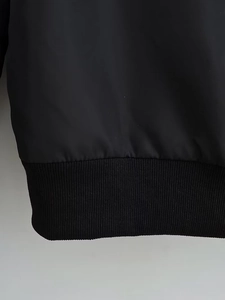 Detailansicht der schwarzen Jacke mit Rippsaum-Nähten und glatter Stoffstruktur