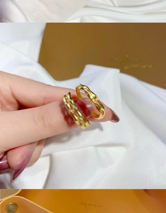 Close-up of gold bow and wheat motif rings worn by a model on silk fabric
