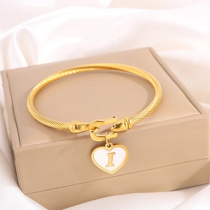 Macro shot of gold twisted cable bangle with heart charm featuring letter I on silk