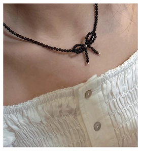 Close-up of a deep red beaded necklace with a bow pendant on a model's collarbone