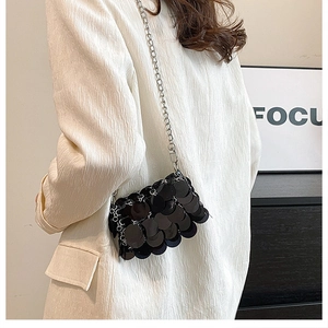 Detail of black sequin crossbody bag with silver chain strap worn over a white blazer