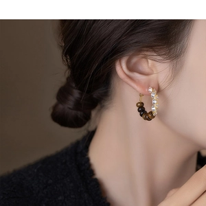 Macro detail of C-shaped gold earrings with tiger eye beads and zircon stones on a model