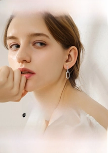 Close-up of elegant silver paperclip earrings with micro-inlaid stones on a female model