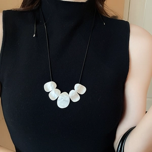 Detail view of irregular white shell pendants on a black leather cord necklace worn by model