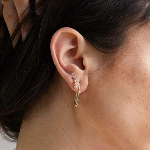 Detailed macro view of a gold safety pin earring and three-stone zircon stud on a model