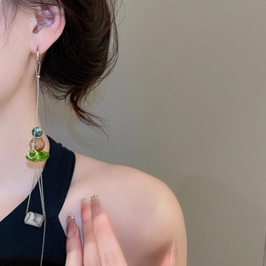 Detailed view of long silver tassel earrings with green beads and ethnic stone charms