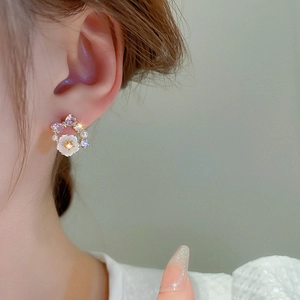 Macro view of gold flower earrings with purple bows and pearls on model ear