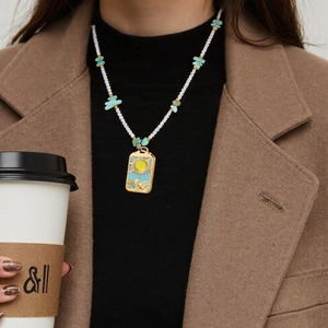 Collier de perles bohème avec pendentif soleil porté par un mannequin en manteau de ville