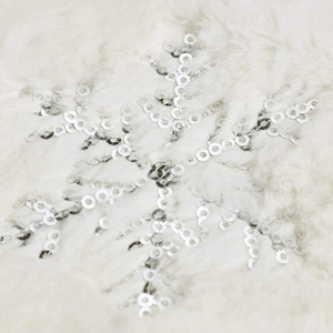 Macro shot of white plush fabric featuring an embroidered silver sequin snowflake detail