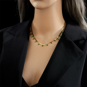 Gold snake chain necklace with green rectangular stones worn over black attire