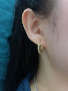 Close-up of a gold s925 silver hoop earring with paved zircon stones on a female ear