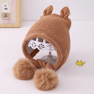 Close-up of knit baby winter hat with plush ear flaps and cute fuzzy ear pom-poms