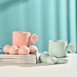 Close-up of cat-paw handle ceramic mug with matching saucer in pink and mint green sets