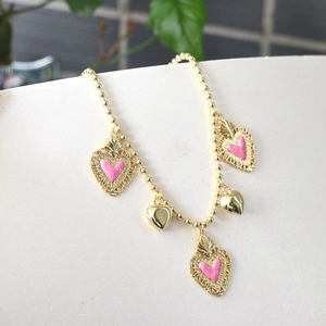 Detail of a beaded gold chain bracelet with pink enamel and hollow floral heart charms