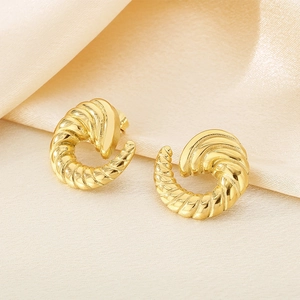 Macro detail of golden spiral twisted croissant earrings on elegant silk background