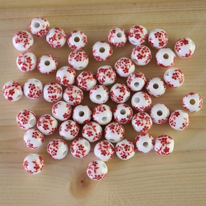Detailed macro shot of round white ceramic beads with red floral patterns for DIY jewelry