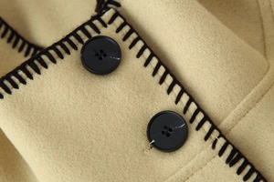 Close-up of beige wool fabric texture with black resin buttons and contrast stitching details