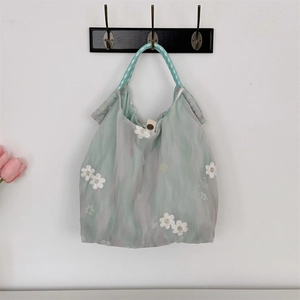Detail of light green tulle tote bag with white flower embroidery and braided handles