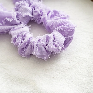 Detailed close-up of purple fabric hair scrunchie with fringe edges on linen background