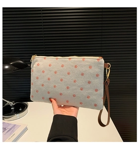 Detail of beige canvas clutch with red floral pattern, wrist strap, and golden zipper