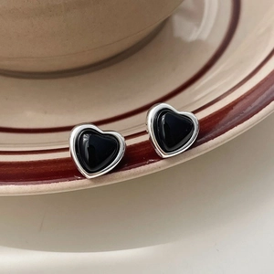 Macro shot of minimalist silver heart studs with black resin inlay on a beige ceramic plate