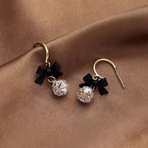 Detail of gold-plated bow earrings with black matte finish and crystal bead on brown satin