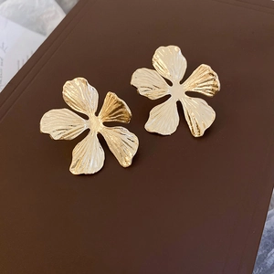 Detail of gold petal earrings with irregular pleated texture on dark background