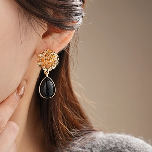 Macro view of vintage gold flower earring with black teardrop pendant on a model
