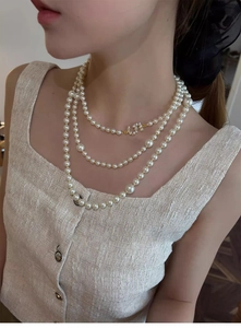 Detail of elegant three-layer pearl necklace with sparkling double C rhinestone pendant