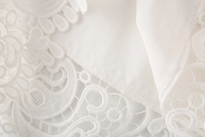 Gros plan sur la broderie de dentelle blanche et la maille ajourée du haut à col V