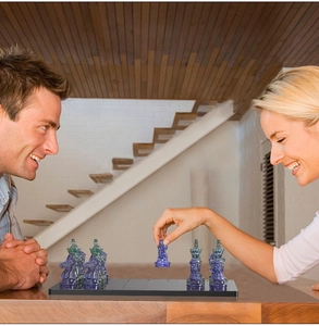 People playing chess with transparent blue and green resin pieces on a modern black board
