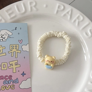 Détail d'un chouchou crème en soie avec ours jaune posé sur une assiette décorative blanche