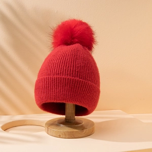 Berretto invernale in maglia rossa con grande pompon in ecopelliccia su supporto in legno