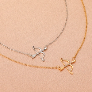Gold and silver cupid arrow pendant necklaces with zircon inlay on warm orange background