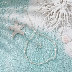 Fashionable double-layer pearl anklet and toe ring set on a sea shell and coral beach background