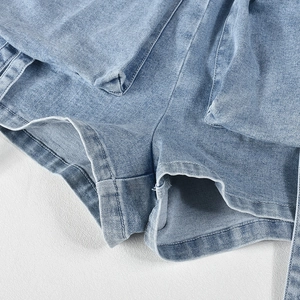 Macro detail of light blue denim romper featuring double-stitched hem and fabric texture