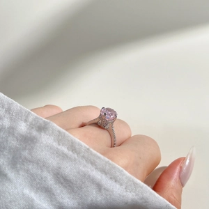Macro shot of an oval pink zircon ring with a halo setting and pavé band on a hand