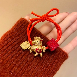 Détail d'un élastique à cheveux rouge avec pendentif cheval doré et perle de chance