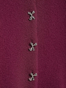 Detail view of burgundy velvet fabric featuring three silver metal bow-shaped buttons