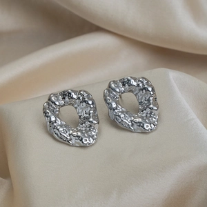 Macro detail of silver irregular textured hoop earrings on soft beige silk fabric