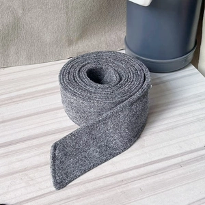 Macro detail of charcoal grey wool belt roll for winter coats on a wooden surface