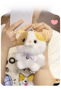 Close-up of calico cat plush keychain with purple bow, silver bell and branded tag