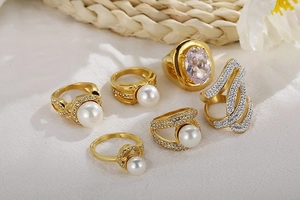 Detailed set of gold plated titanium rings with pearls and zircon crystals on table