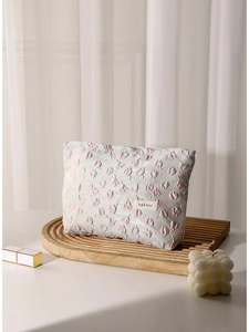 Floral embossed cosmetic bag in off-white and pink on wooden tray with soft lighting
