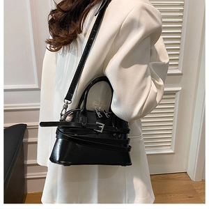 Detail of a black glossy leather shell bag with silver hardware on a white blazer