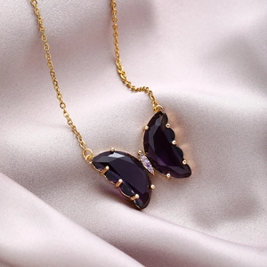 Close-up of gold butterfly necklace with purple crystal wings on soft satin background