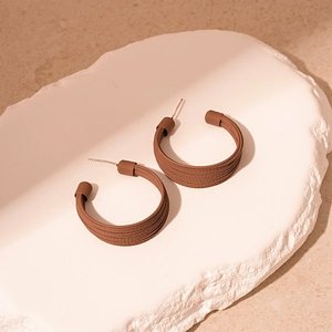 Detailed view of dark brown C-shaped earrings with fine striped texture on stone tray