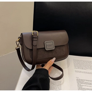 Detail of dark brown shoulder bag with gold hardware and suede stitching on book background