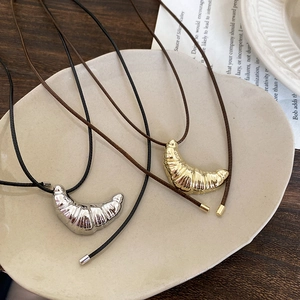 Detail showing gold and silver croissant pendants on black cords over a ceramic plate